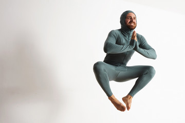Happy smiling bearded young athlete wearing thermal baselayer suite and jumping like a ninja in air, isolated on white