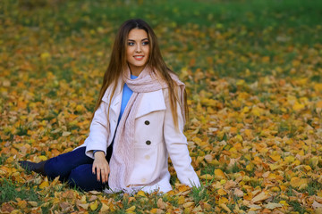 Young woman smiling sitting on the grass in the autum. fall yellow maple garden background.