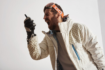 Man in snowboard gear with googles on head screaming into walkie talkie