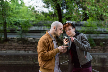 Two young caucaisan man and woman outdoor in the city using smart phone hand hold, talking and smiling - technology, social network, freindship concept