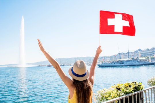Young female traveler with swiss flag enjoying great view on Geneva lake with famous fountain in Switzerland