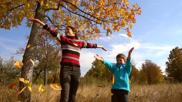 Two kids throwing up the autumn leaves, slow motion