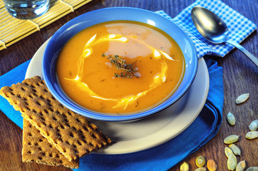 Pumpkin cream-soup.  Hot pumpkin soup with sour cream and pumpkin seeds in a blue bowl on a wooden table. Healthy food still life