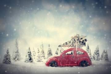 Fototapeta na wymiar Retro toy car carrying tiny Christmas tree. Fairytale scenery with snow and forest.