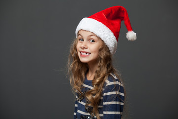 Profile portrait of a cute little girl in a christmas cap, gray background
