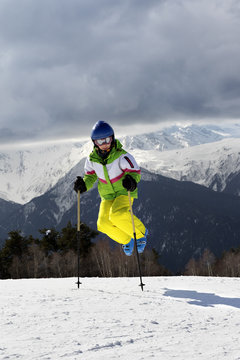 Young skier jump with ski poles in sun winter mountains and clou