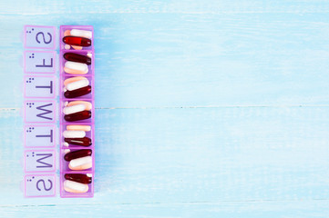 variety of pills in blue plastic pill organizer on weathered wood