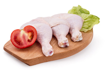 Fresh raw chicken legs arrangement on kitchen cutting board with lettuce and tomato