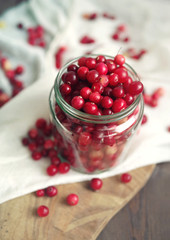 Fresh berries of a cranberry in a glass jar among the scattered berries on white linen fabric on a wooden surface of a table