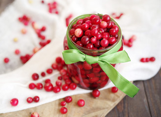 Fresh berries of a red cranberry in a glass jar the decorated green tape among the scattered berries on white linen fabric