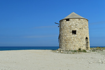 Fototapeta na wymiar Old abandoned stone-built windmill on the beach of Lefkada, Greece