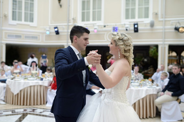 Wedding couple in the restaurant is dancing. Beautiful model girl in white dress. Handsome man in suit. Beauty bride with groom. Female and male portrait. Woman with lace veil. Lady and guy indoors