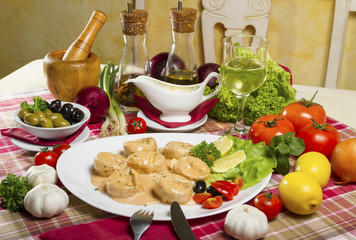 Salmon tortellini in sauce served on a white plate with lemon, olives, cherry tomatoes and parsley next to fresh vegetables, olive oil, white wine and mortar and pestle.