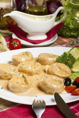 Salmon tortellini in sauce served on a white plate with lemon, olives, cherry tomatoes and parsley.