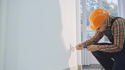 Man wearing brown shirt and dungarees working on electrical wall socket wires using screwdriver, electrician concept.