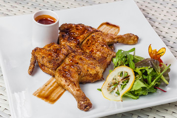 Chicken tabaka with sauce and lettuce on a white plate