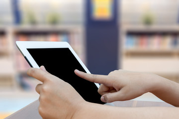 Close-up hand using digital tablet on blurred library background