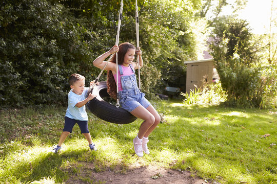 Brother Pushing Sister On Tire Swing In Garden