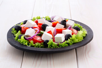 Greek salad with fresh vegetables on wooden background, feta cheese and black olives. Love for healthy raw food concept.