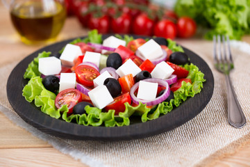 Greek salad with fresh vegetables on wooden background, feta cheese and black olives. Love for healthy raw food concept.