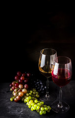 Wine in glasses and different types of grape on dark background.
