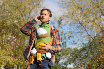father with baby in colorful sling talking on a mobile phone
