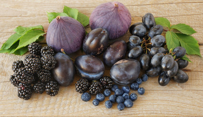 Blue and purple food. Blackberries, grapes, plums, blueberries, figs on a wooden background. Tasty and ripe fruits and berries.