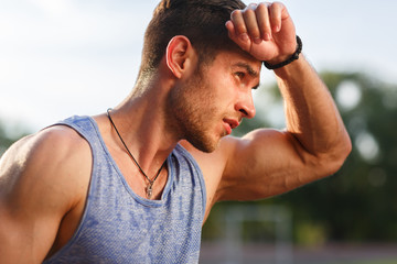 Portrait of fatigued fitness guy on hot sunny day