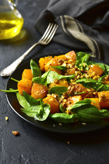 Roasted pumpkin salad with spinach and walnut on a black plate.
