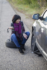 a woman changing a wheel on a car on the empty road