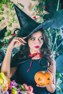 HalloweenWitch with a magic Pumpkin. Beautiful young woman in witches hat and costume holding carved Jack lantern pumpkin