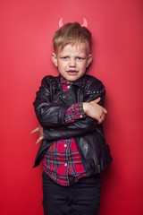 Little handsome devil with horns and tail. Kid. Halloween. Studio portrait isolated over red background