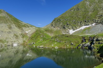 Beautiful view of high mountain lake. Landscape from Capra Lake in Romania and Fagaras mountains in the summer.