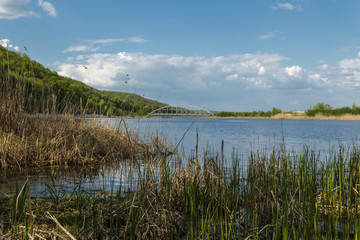 A beautiful Blue Lake with yellow grass in the foreground and a blue sky with clouds