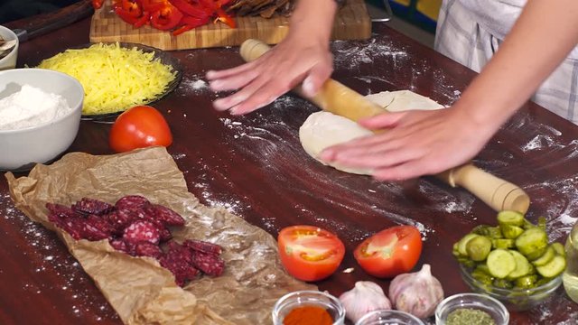 Women kneading dough for pizza in flour on table