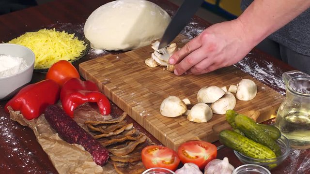 Mens hands cut mushrooms on bamboo cutting board for cooking pizza. Pizza ingredients on wooden background
