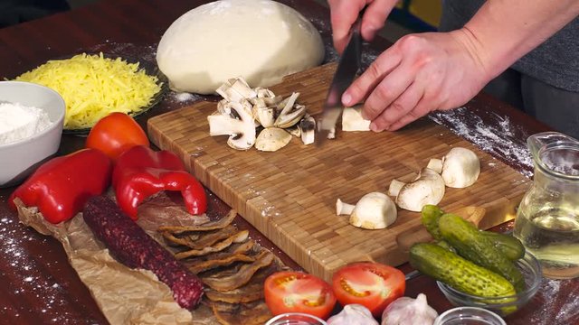 Mens hands cut mushrooms on bamboo cutting board for cooking pizza. Pizza ingredients on wooden background