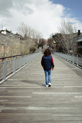 Girl walking in the footbridge in the city with wooden floor and steel. Rear view