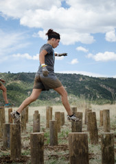 Female competitor trying to keep her balance running across three foot tall wooden stumps on a beautiful cloudy blue sky day