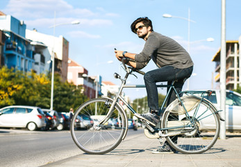 Young handsome guy with a bicycle on street, he is holding mobile phone.