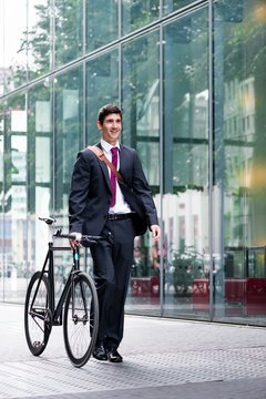 Businessman wheeling a bicycle through town