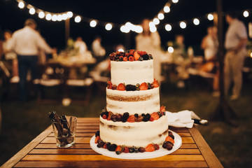 three-level white wedding cake decorated with cream and berries, stands on a table in the banquet...