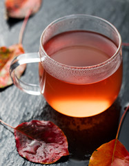Cup of tea, autumn leaves on wet stone background