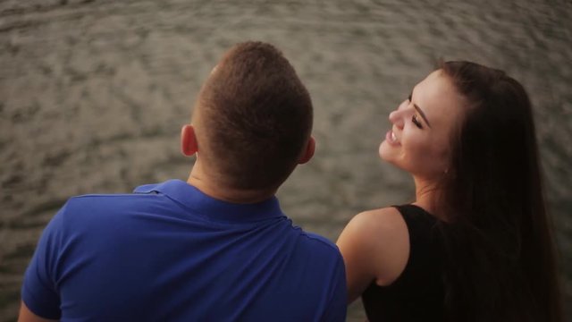 Portrait of a happy beautiful young couple man and woman kissing outdoors on the bright sunny day near the water