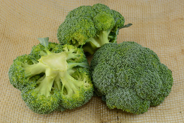Three raw uncooked broccoli heads on burlap
