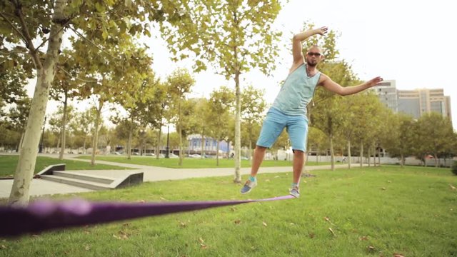 Guy walks on slackline at public park