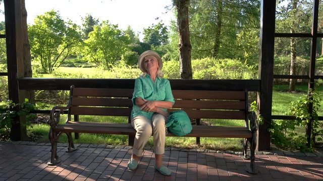 Mature woman is smiling. Lady sits on park bench. Medication has no side effects. Heart pains are gone.