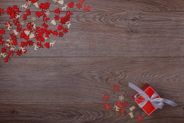 Christmas decorations on wooden background with copy space for text. Red-white chaotic small ornaments on the left and red gift box on the right. Top view.