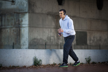 Attractive young man is enjoying his favorite music while jogging on city street.