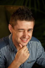 Naklejka premium Emotion wink. Young man holds his chin and winks at the camera